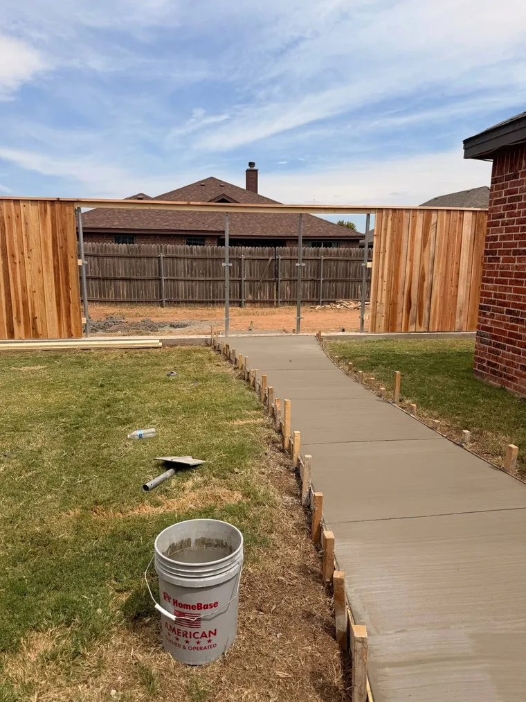 New concrete backyard sidewalk with control joints leading to a cedar fence gate
