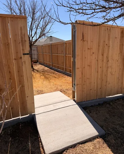 Cedar fence with a walk gate opening onto a new concrete sidewalk, built on steel posts and a curb