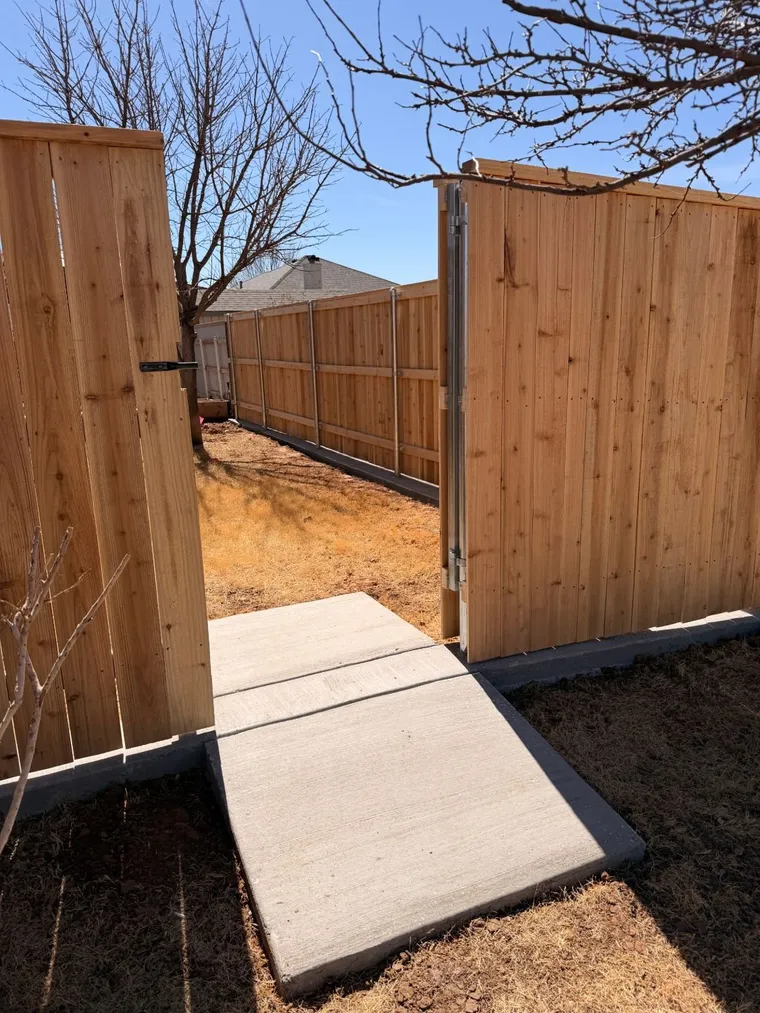 Cedar fence with a walk gate opening onto a new concrete sidewalk, built on steel posts and a curb