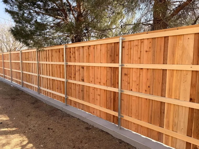 Back side of a capped cedar fence showing steel posts and three rails on a concrete curb
