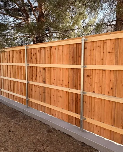 Back side of a capped cedar fence showing steel posts and three rails on a concrete curb