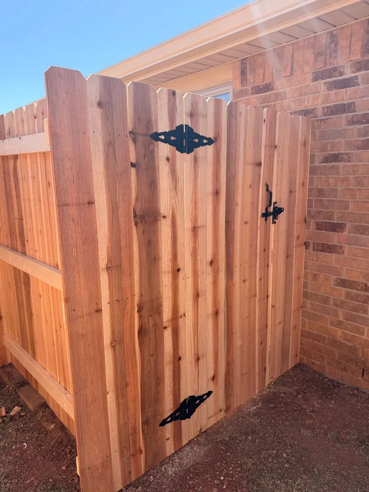 Dog ear cedar walk gate with black hinges beside a brick home