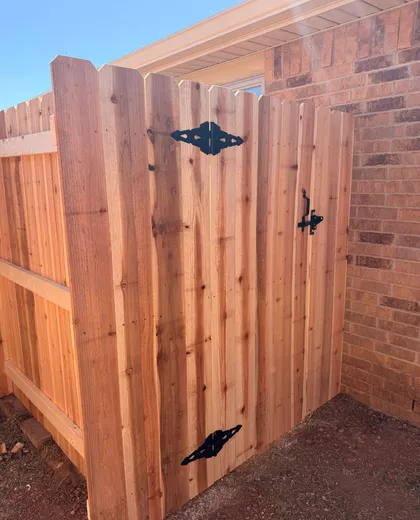Dog ear cedar walk gate with black hinges beside a brick home