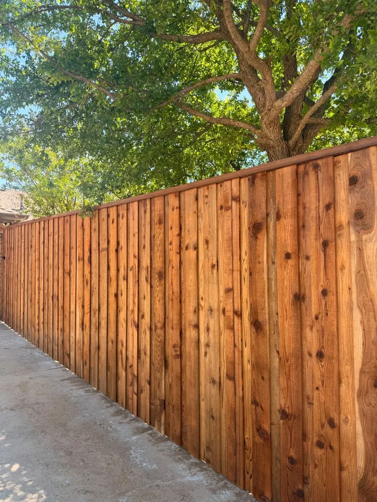 Stained capped cedar fence along a concrete patio under a shade tree