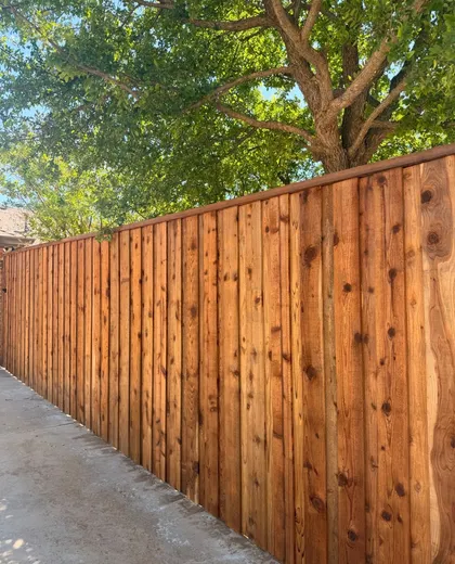Stained capped cedar fence along a concrete patio under a shade tree
