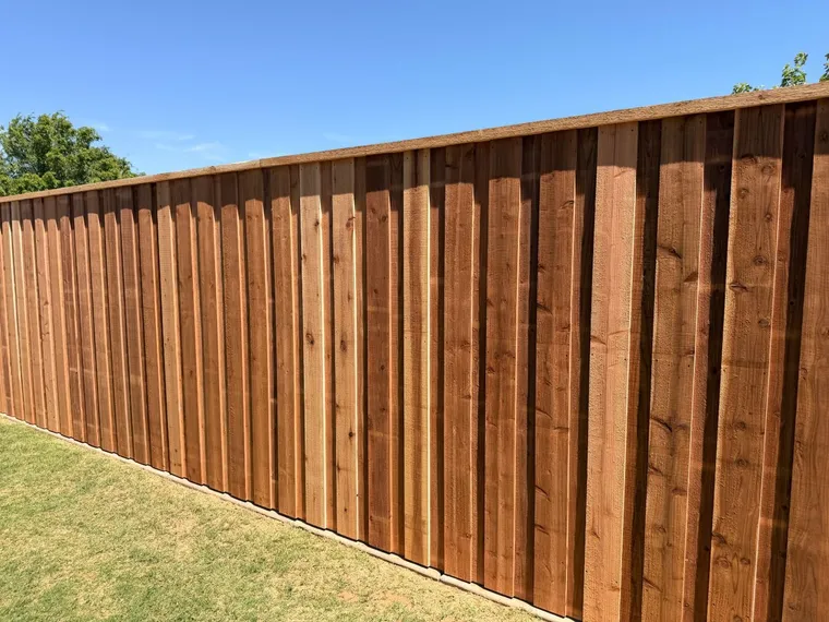 Freshly stained capped cedar board-on-board fence across a green backyard