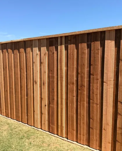 Freshly stained capped cedar board-on-board fence across a green backyard