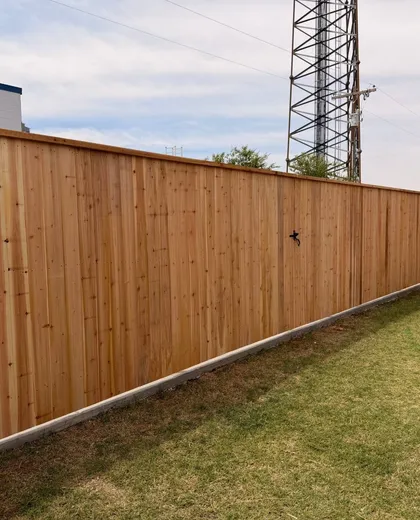 Long capped cedar privacy fence on a concrete curb beside a commercial building