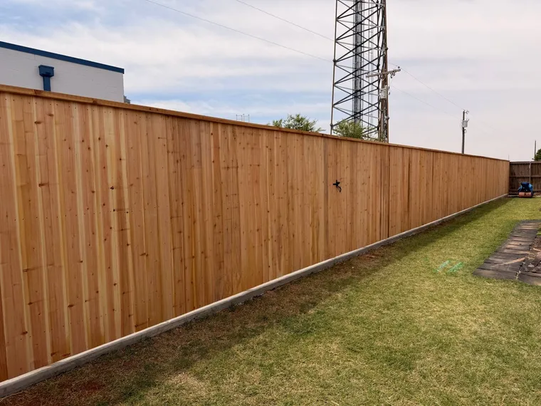 Long capped cedar privacy fence on a concrete curb beside a commercial building