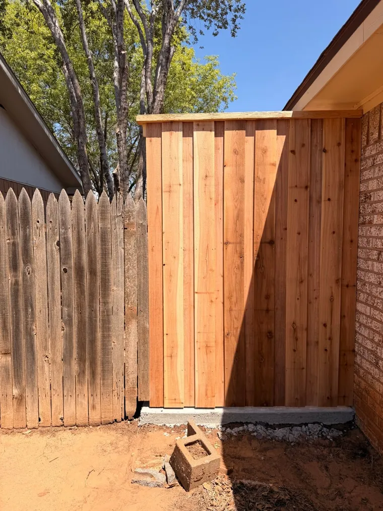 New capped cedar fence section on a curb next to an old neighbor fence