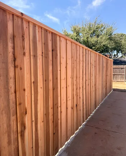 Capped cedar board-on-board fence running along a concrete patio