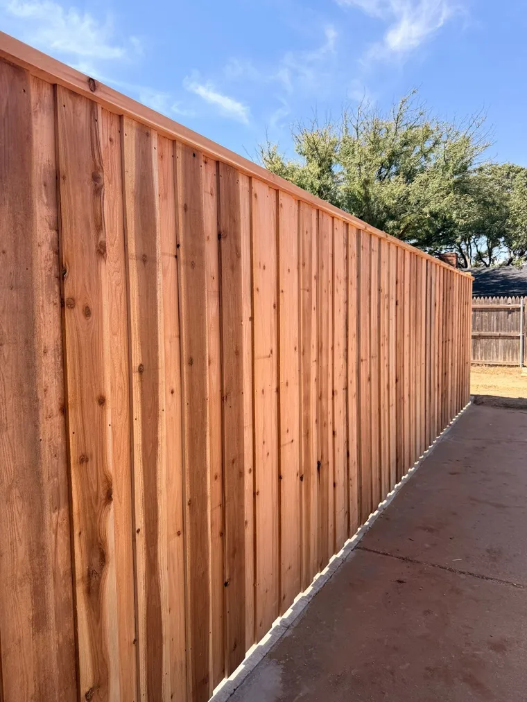 Capped cedar board-on-board fence running along a concrete patio