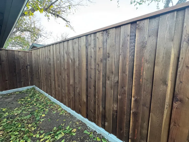 Dark stained capped cedar board-on-board fence on a concrete curb