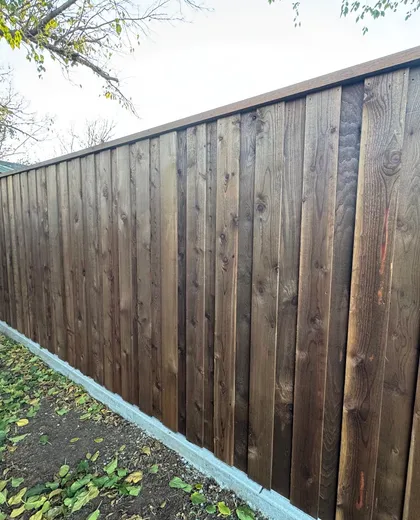 Dark stained capped cedar board-on-board fence on a concrete curb