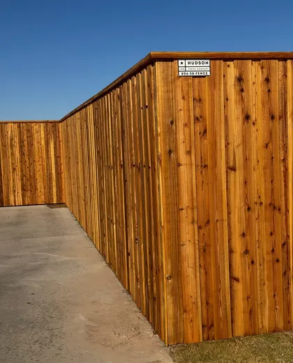 Stained capped cedar fence with a Hudson Fence Company sign along a patio