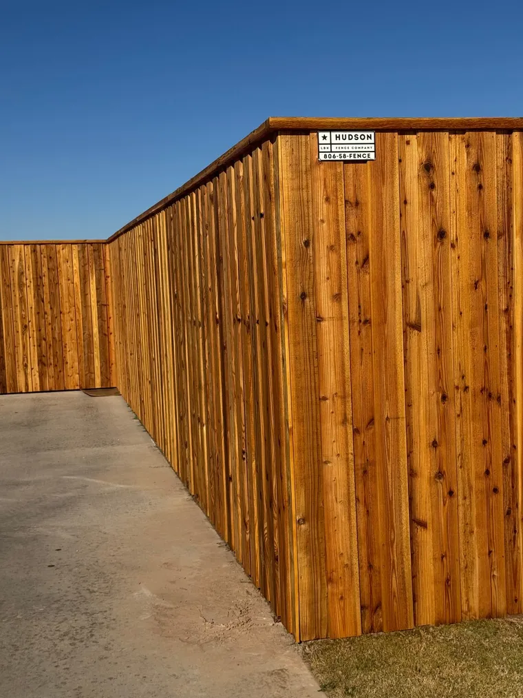 Stained capped cedar fence with a Hudson Fence Company sign along a patio