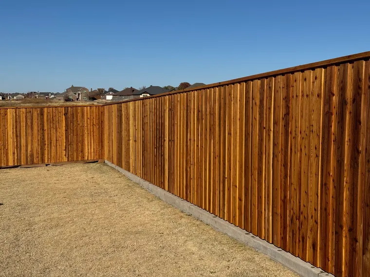 Stained capped cedar board-on-board fence on a concrete curb in a new neighborhood
