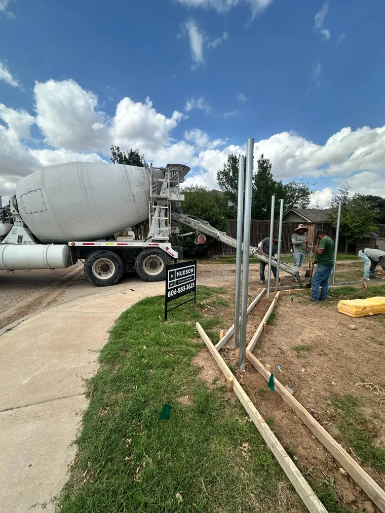 Hudson Fence Company crew pouring a concrete fence curb from a ready-mix truck in Lubbock, TX