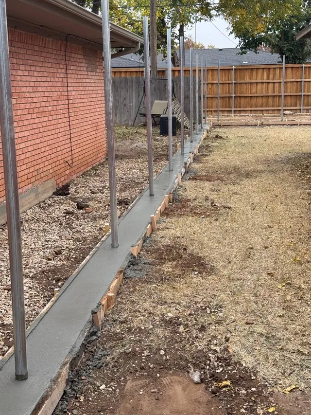 Freshly poured concrete fence curb with steel posts set in it, ready for a new fence