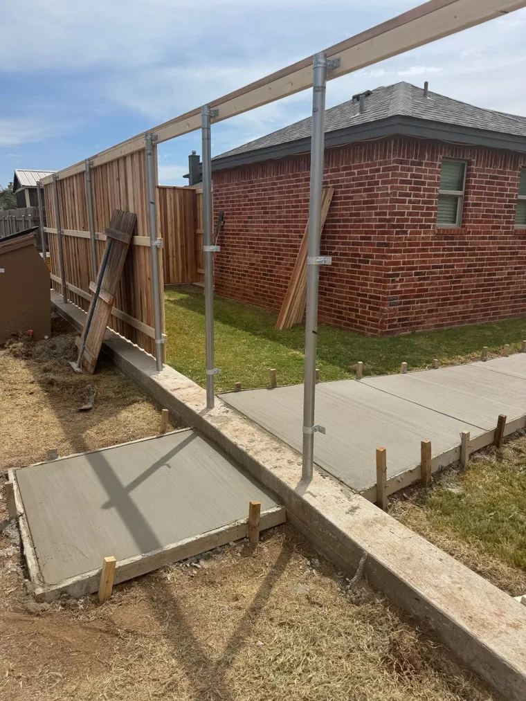 New concrete sidewalk and pad poured alongside a fence curb and new cedar fence