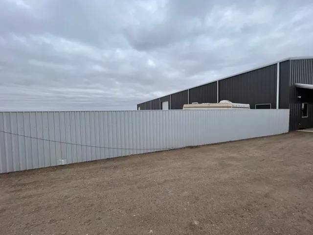 Finished side of a long R-Panel steel privacy fence beside a metal shop building near Lubbock, TX