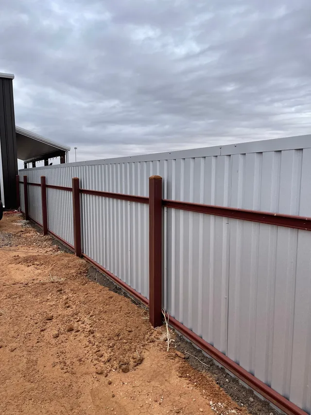 Back side of an R-Panel fence showing square steel posts, steel rails, and top trim