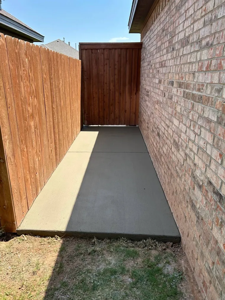 Concrete side yard slab between a brick home and a stained cedar fence